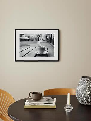 Black framed black-and-white print of a steaming coffee cup above a round table