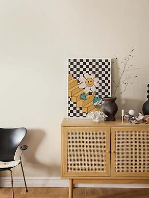 Plakat med smilende blomst på ternet baggrund, lænet på skænk med vase og dekorationer