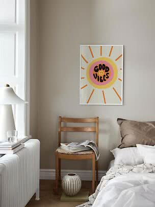 Gerahmtes Good Vibes Poster mit Sonnenmotiv über einem Holzstuhl im hellen Schlafzimmer