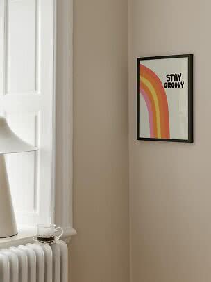 Gerahmtes Retro-Poster mit Regenbogenbögen und dem Text "Stay Groovy" an beigefarbener Wand