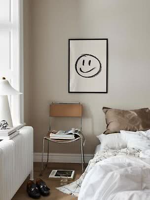 Poster con smiley in cornice nera sopra una sedia in una camera beige