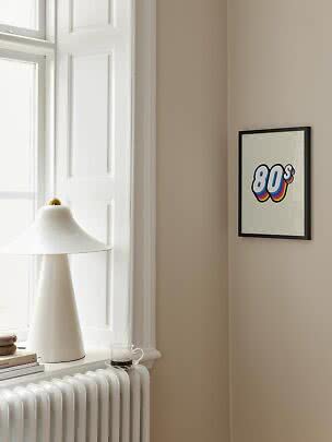 Stampa incorniciata con scritta colorata '80s' su parete beige accanto a finestra e lampada bianca