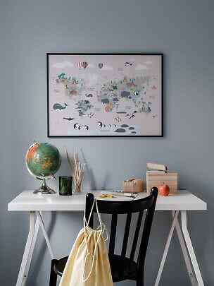 Carte du monde encadrée avec animaux au-dessus d’un bureau blanc avec globe et accessoires