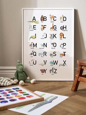 Framed animal alphabet poster leaning against a nursery wall, with plush toy and prints on the floor
