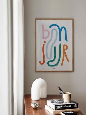 Inramad abstrakt poster med färgstarka bokstavsformer ovanför ett träbord med böcker och dekoration