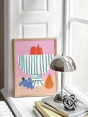 Indrammet frugtillustration med skål, druer og pære på vindueskarm ved siden af kromlampe