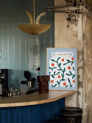 Framed Valencia poster with oranges on a bar counter in a rustic cafe interior