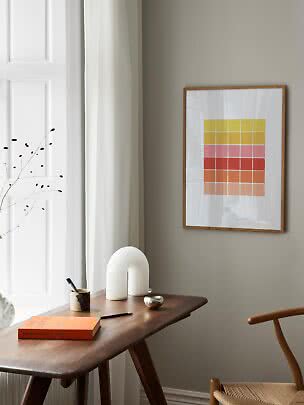 Framed abstract print with colored blocks hanging above a wooden desk by a window