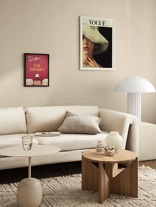 Lys stue med hvid sofa, sofaborde, lampe og to indrammede plakater på beige væg