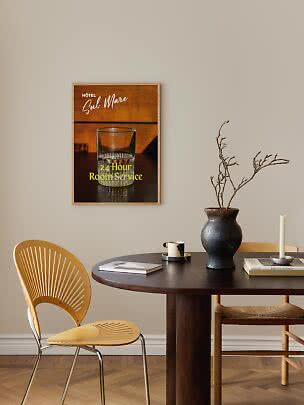 Poster hotel incorniciato con bicchiere e scritta "24-Hour Room Service" sopra un tavolo scuro