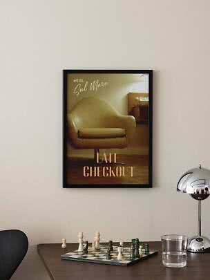 Affiche vintage encadrée avec fauteuil et texte « Late Checkout » sur mur clair au-dessus d’un échiquier