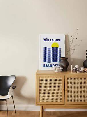 Poster met blauwe golven en gele zon op houten dressoir met vaas en decoratie