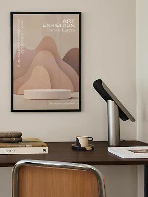 Framed art poster with soft curved beige and pink shapes on a wall above a desk