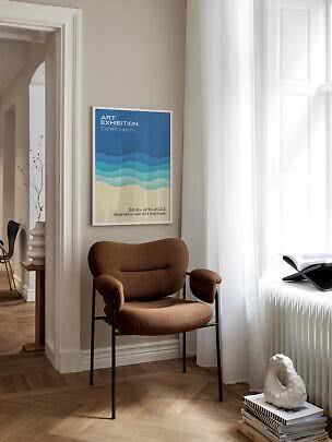 Affiche d’art bleue et beige en cadre blanc au-dessus d’un fauteuil brun près d’une fenêtre