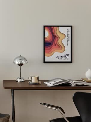 Framed art exhibition poster with wavy colors above a desk with lamp, mug, and open book
