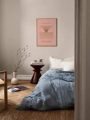 Gerahmtes rosa Poster über einem Bett mit blauer Bettwäsche in ruhigem Schlafzimmer