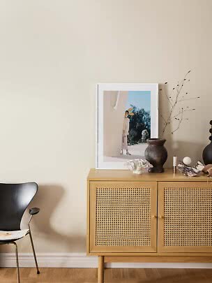 Licht houten dressoir met rotan deuren, vaas, decoratie en ingelijste print tegen beige muur