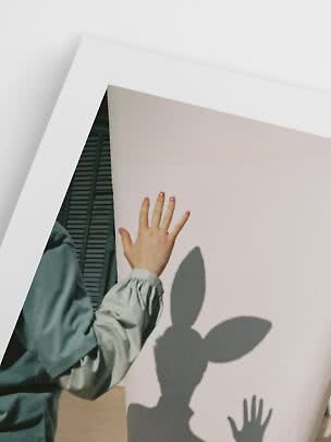 Mano con blusa verde claro frente a un gran panel blanco con sombras de hojas y mano
