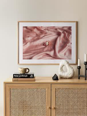 Affiche encadrée montrant du satin rose et un petit fruit, au-dessus d’un meuble en bois