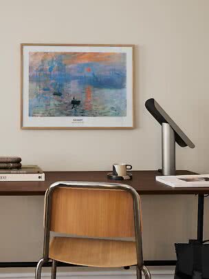 Affiche encadrée de Monet au-dessus d’un bureau avec lampe, livres, tasse et chaise en bois