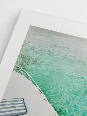 Foto enmarcada de un barco sobre agua turquesa apoyada en una pared blanca