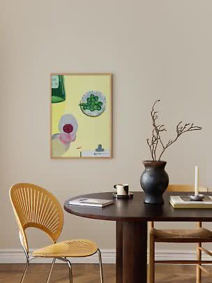 Essecke mit rundem dunklem Tisch, Stuhl, schwarzer Vase mit Zweigen und buntem Wandbild