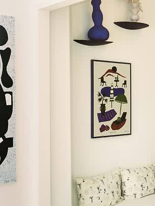 Cozy corner with framed art, wall shelves with vases, and a sofa with patterned cushions