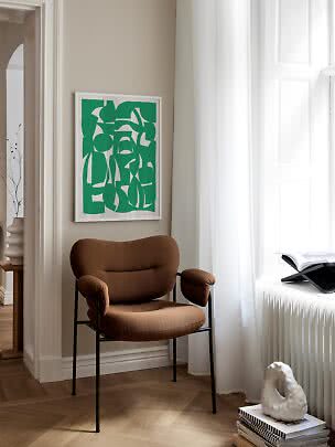 Brauner Polsterstuhl mit schwarzen Beinen am Fenster unter einem grünen abstrakten Bild