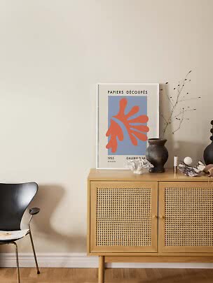 Light wood sideboard with cane doors, vase, art print and chair against a beige wall