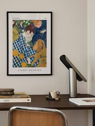 Indrammet Pierre Bonnard-plakat over skrivebord med lampe, bøger og kop