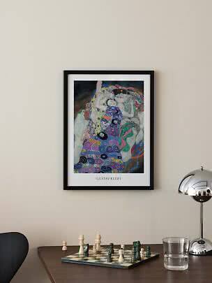 Gerahmtes Gustav-Klimt-Poster über einem Tisch mit Schachbrett, Wasserglas und Chromlampe