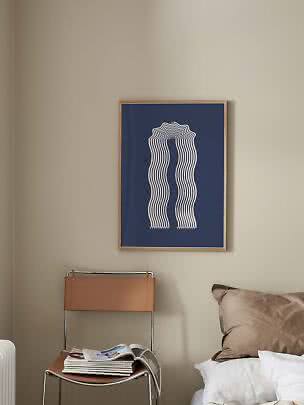 Poster blu incorniciato con linee ondulate bianche sopra una sedia in pelle accanto al letto