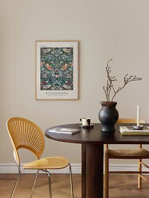 Inramad William Morris-affisch med fåglar och blommor ovanför ett mörkt matbord med vas och ljus.