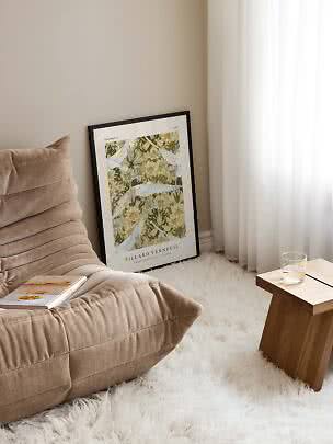 Indrammet kunstplakat med fugle og blomster læner op ad væggen ved en beige loungestol.
