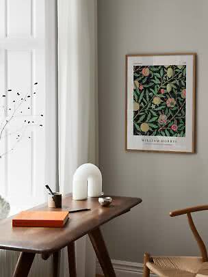 Indrammet William Morris-plakat med frugt- og bladmønster på grå væg over træskrivebord