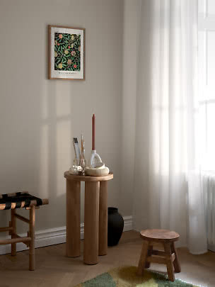 Lyst hjørne med rundt træbord, lysestage, små dekorationer og botanisk plakat på væggen