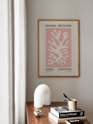 Framed pink art print above a wooden table with books, a sculptural vase, and a mug