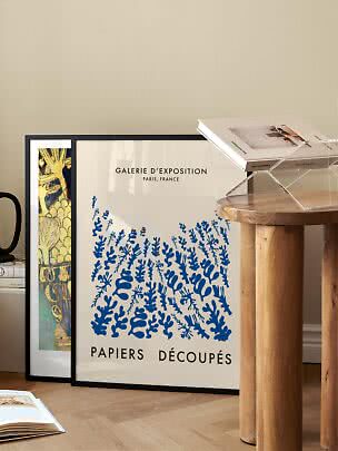 Framed poster with blue abstract motif leaning by a wall beside a wooden table and acrylic book stand