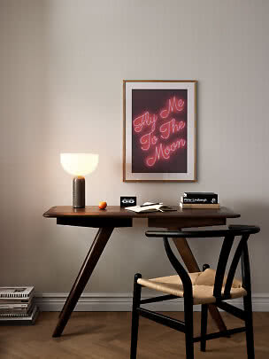 Mörkt träskrivbord med stol, bordslampa, böcker och poster med rosa neontext på väggen