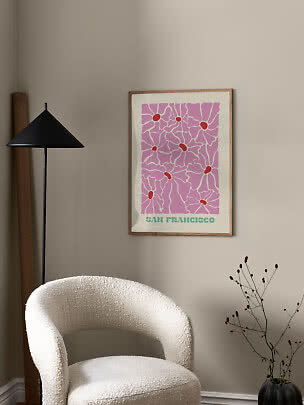 Ingelijste San Francisco-poster met roze bloemenpatroon aan beige muur boven witte fauteuil