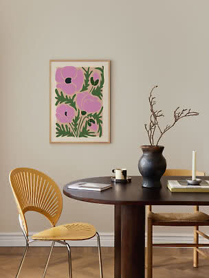 Stampa floreale incorniciata con fiori rosa e foglie verdi sopra un tavolo da pranzo scuro