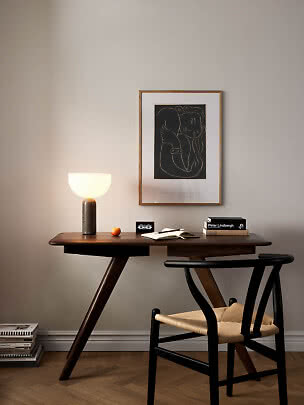 Scrivania in legno scuro con lampada accesa, libri, taccuino e sedia nera sotto un quadro.
