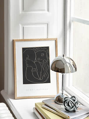 Poster di Matisse incorniciato su davanzale accanto a lampada da tavolo cromata e libri impilati