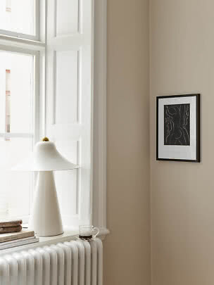 Lampe de table blanche sur un rebord de fenêtre lumineux, avec livres, tasse et cadre sur mur beige
