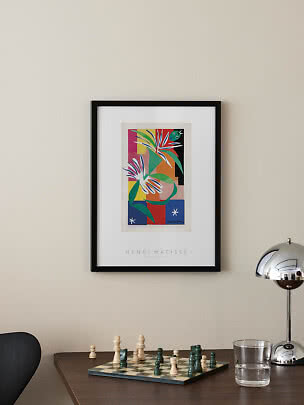 Indrammet Henri Matisse-plakat med farverigt motiv hængt over bord med skakbræt og kromlampe