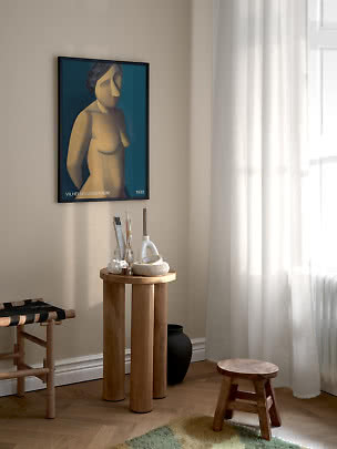 Poster d’arte incorniciato con figura femminile astratta su parete beige in un angolo luminoso.