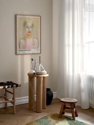 Gerahmter Kunstdruck mit Frauenporträt an beigefarbener Wand über kleinem rundem Holztisch