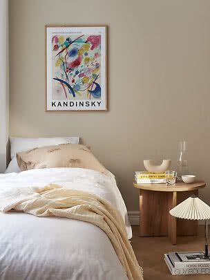 Gerahmtes Kandinsky-Poster mit farbigem abstraktem Motiv über einem Bett in einem beigen Schlafzimmer