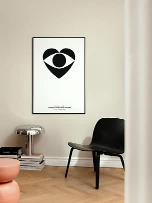 Poster minimalista con motivo a occhio nero in cornice nera su parete chiara sopra una sedia