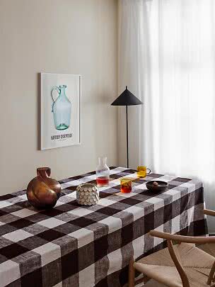 Esstisch mit braun karierter Tischdecke, Glasvasen, Karaffe, Tassen und schwarzer Stehlampe